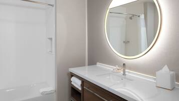 Une salle de bain moderne avec un lavabo blanc, un miroir rond doté d’un éclairage et une douche à parois de verre.