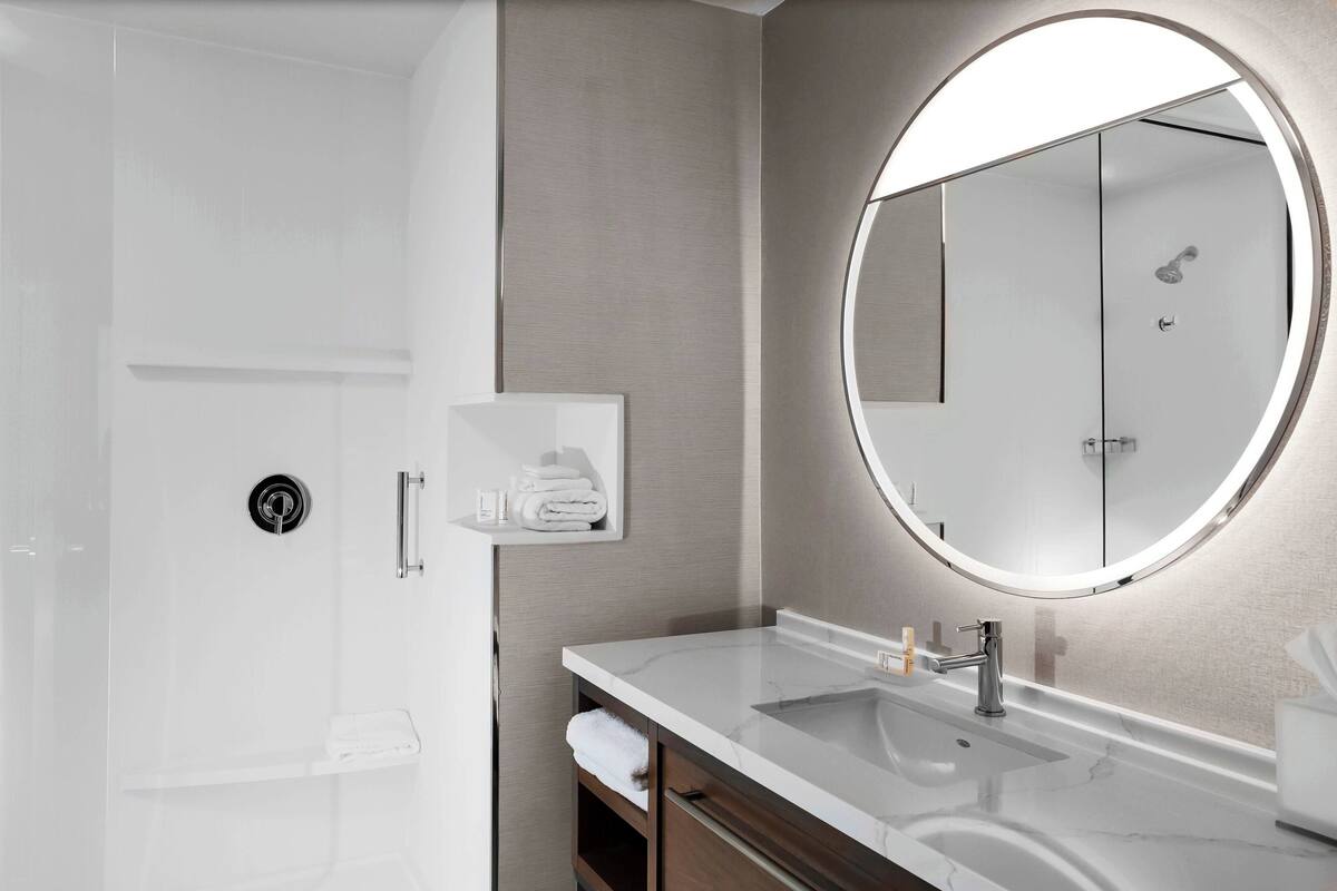 Un baño moderno con cabina de ducha, un espejo grande y un mueble de tocador con lavabo y toallero.