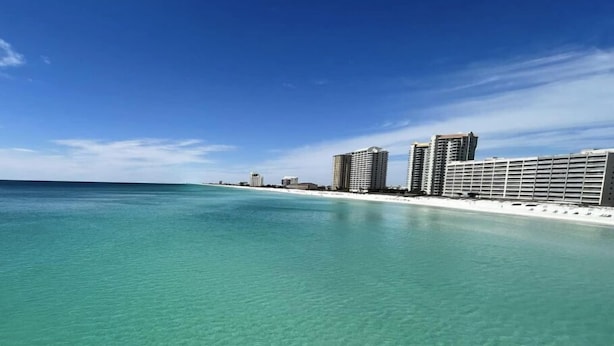 A beachfront hotel with clear turquoise water, a sandy beach, and high-rise buildings in the background.