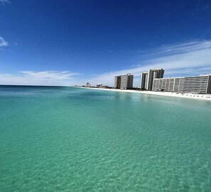 A beachfront hotel with clear turquoise water, a sandy beach, and high-rise buildings in the background.