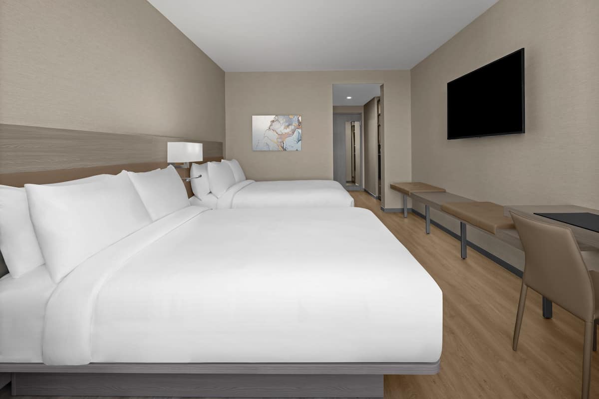 Ein Hotelzimmer mit zwei Betten, einem Schreibtisch, einem Stuhl, einem Fernseher und einem Bild an der Wand.