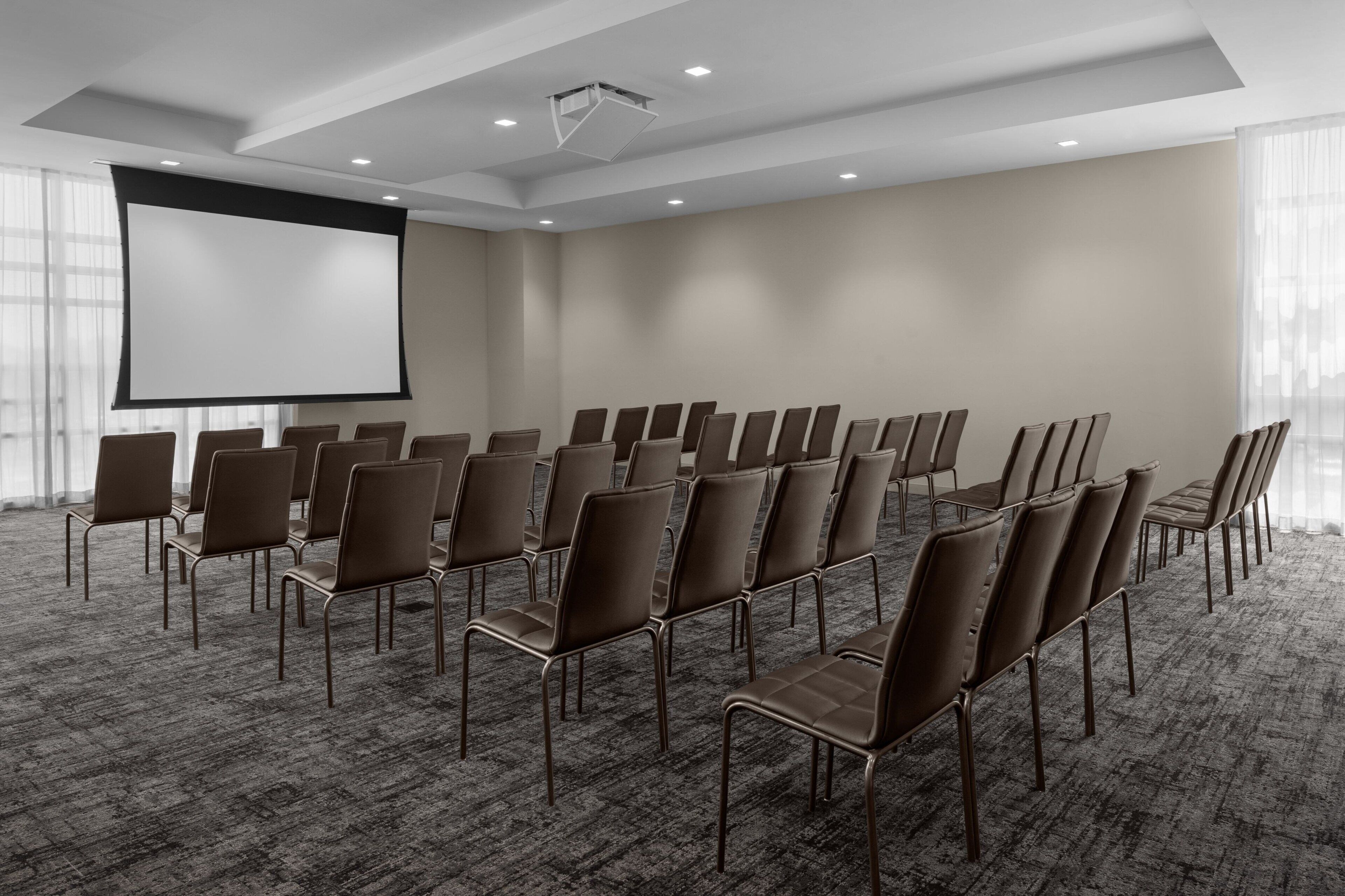 Un salón de conferencias con filas de sillas, una pantalla grande y piso alfombrado.