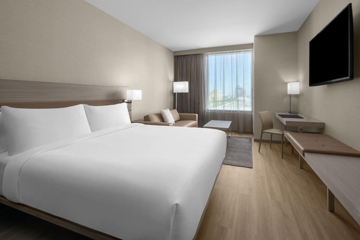Ein Hotelzimmer mit einem großen Bett, einem Schreibtisch, einem Stuhl und einem an der Wand befestigten Fernseher.