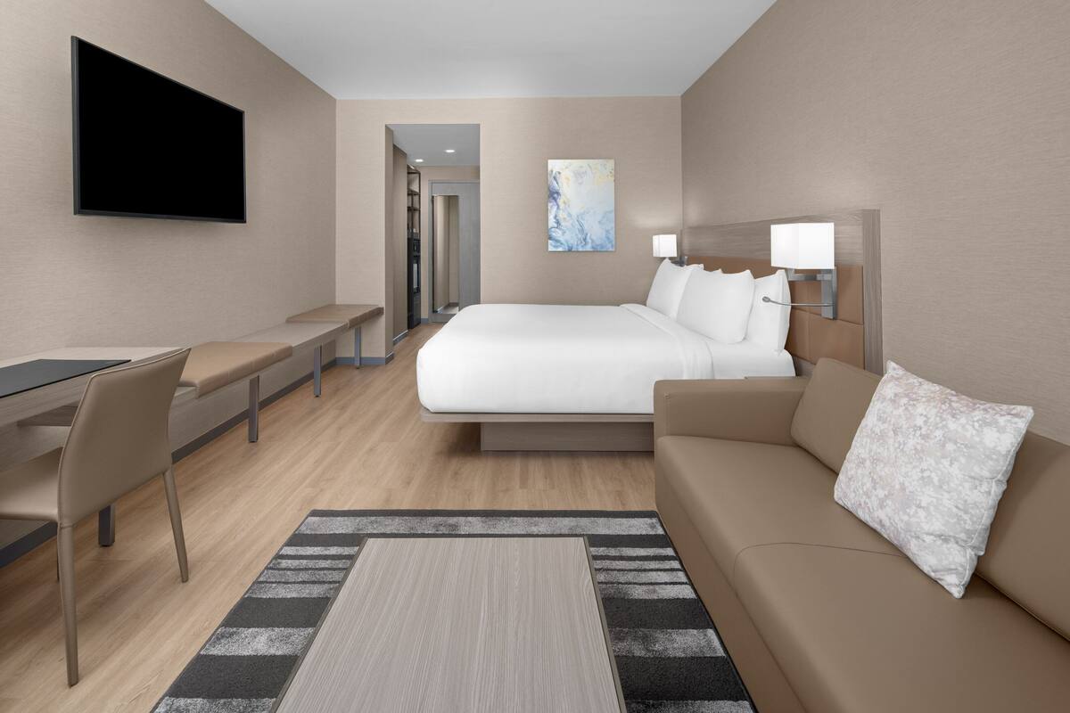 Ein modernes Hotelzimmer mit einem Bett, einem Schreibtisch, einem Sessel, einer Couch, einem Flachbildfernseher und einem Bild an der Wand.