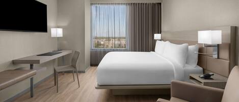 Una habitación de hotel moderna con una cama grande, un escritorio, una silla y un televisor montado en la pared.