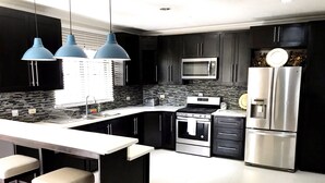 A modern kitchen with dark cabinetry, stainless steel appliances, a central island with bar stools, and pendant lighting.