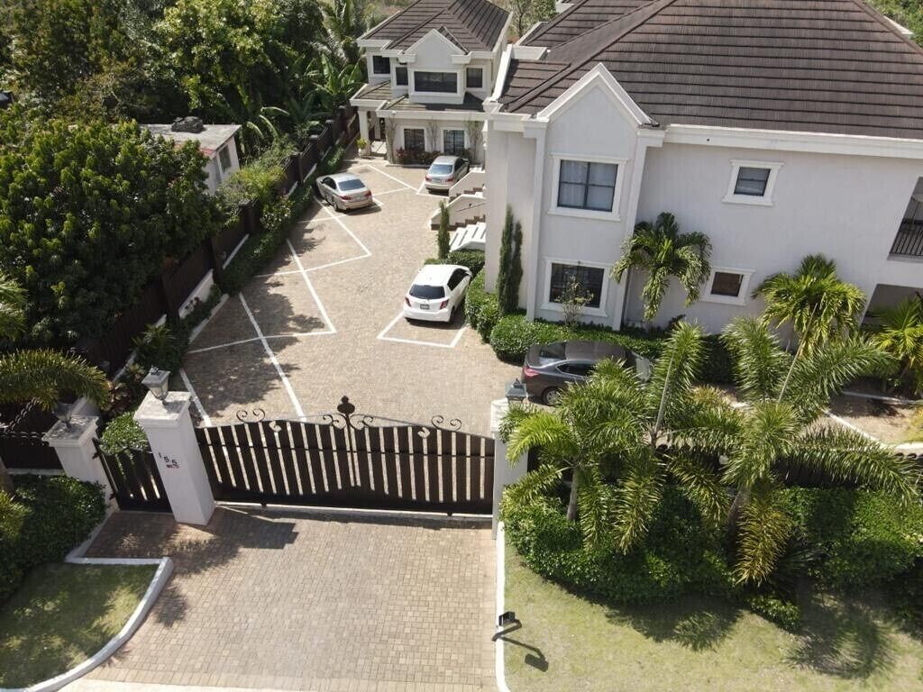 A gated residential area with multiple houses, a parking lot, and lush greenery.
