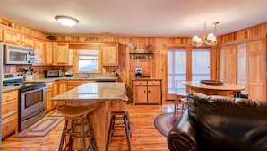 A wooden cabin-style kitchen with a central island, bar stools, a dining table, and a leather couch. - River Roost - on New River near Boone with fire pit, game room, pet friendly (Todd)