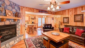 A cabin interior with a stone fireplace, wooden walls, a dining area, and a leather sofa. - River Roost - on New River near Boone with fire pit, game room, pet friendly (Todd)