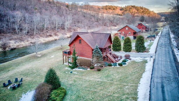 A red barn with a porch and a small deck, surrounded by a grassy area and a river. - River Roost - on New River near Boone with fire pit, game room, pet friendly (Todd)