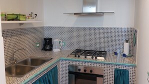 A compact kitchen with a gas stove, oven, and stainless steel sink. There is a patterned backsplash and teal curtains. - VILLA ROSINELLA WITH SEA VIEW (Amalfi)