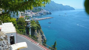 A coastal town with buildings along the cliffside, a road with a guardrail, and boats on the sea. - VILLA ROSINELLA WITH SEA VIEW (Amalfi)