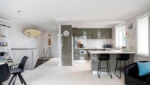Uma cozinha moderna com uma ilha central, eletrodomésticos de aço inoxidável e uma área de refeições com cadeiras pretas.