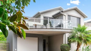 Uma casa moderna de dois andares com varanda, janelas grandes e um pequeno jardim.