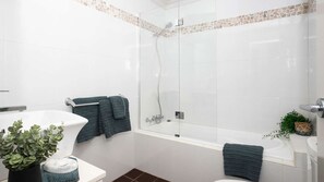 Et moderne badeværelse med brusekabine i glas, et hvidt badekar og et toilet.