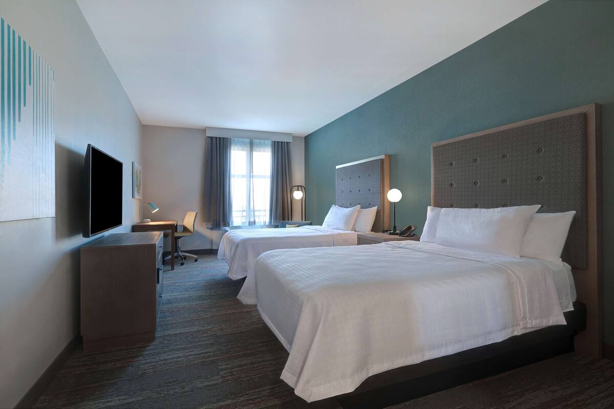 A hotel room with two beds, a desk, a chair, a TV, and a window with curtains.