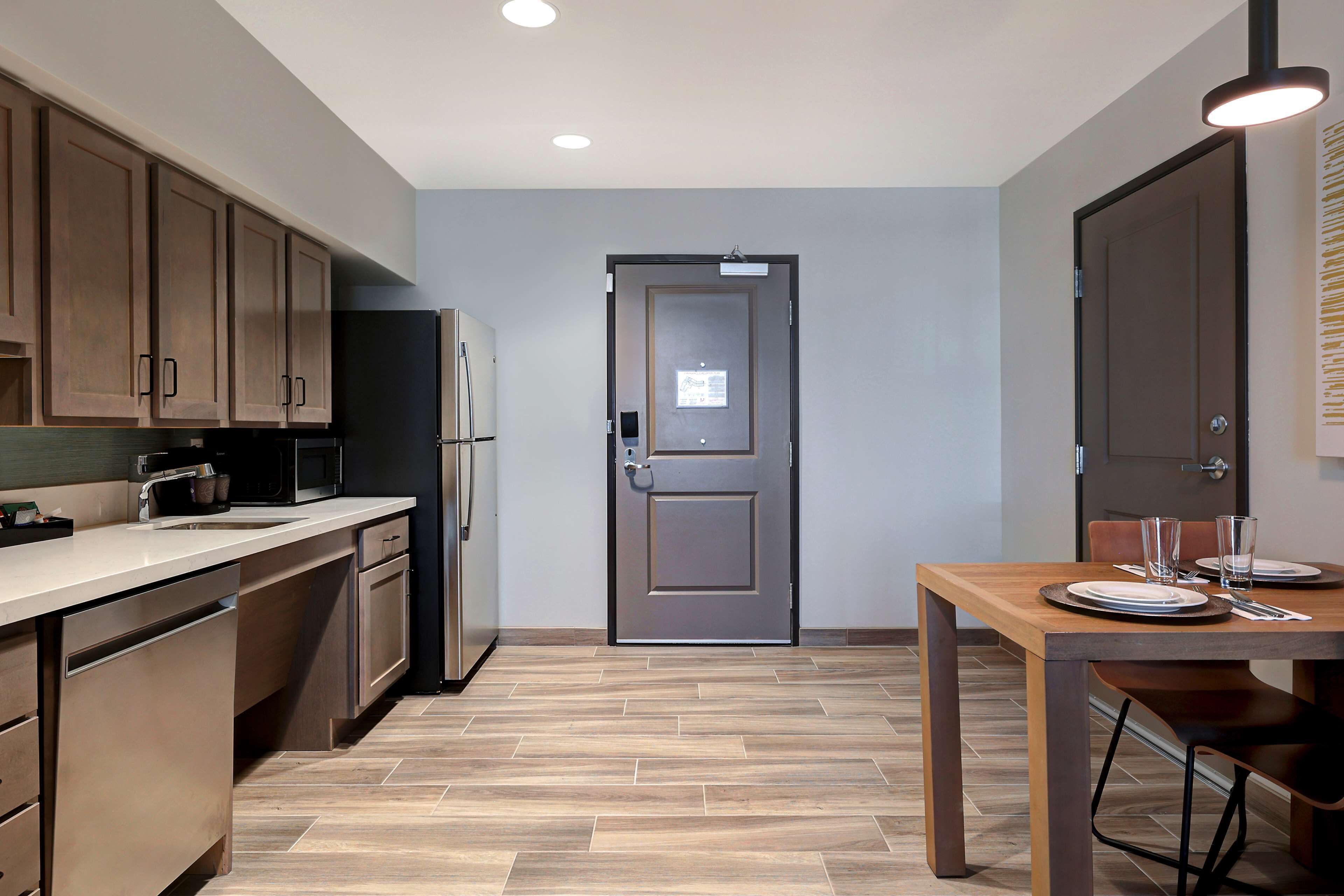 Una cocina moderna con armarios de madera, un refrigerador de acero inoxidable y un comedor con una mesa dispuesta para dos.