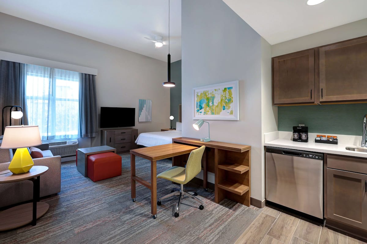 A hotel room with a bed, a desk, a chair, a lamp, a television, a coffee maker, and a dishwasher.