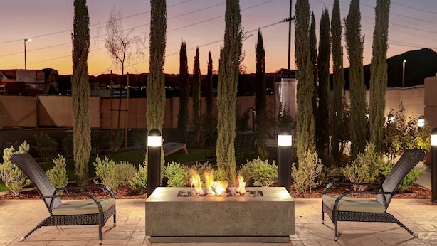An outdoor seating area with a fire feature, two chairs, and tall cypress trees.