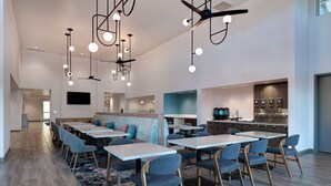 A modern dining area with multiple tables and chairs, a kitchen area with appliances, and a seating area with a sofa and cushions.