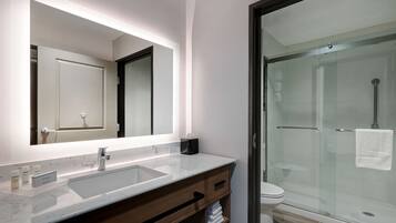 Un baño moderno con un espejo grande, un lavabo con encimera de mármol, cabina de ducha de vidrio y un inodoro.