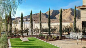 A well-maintained outdoor area with a green lawn, a metal bench, and tall cypress trees.