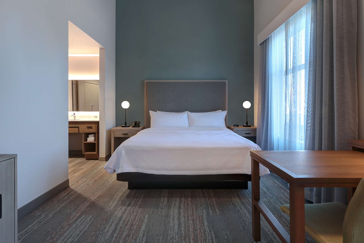 A hotel room with a large bed, bedside tables, a desk, and a window with curtains.