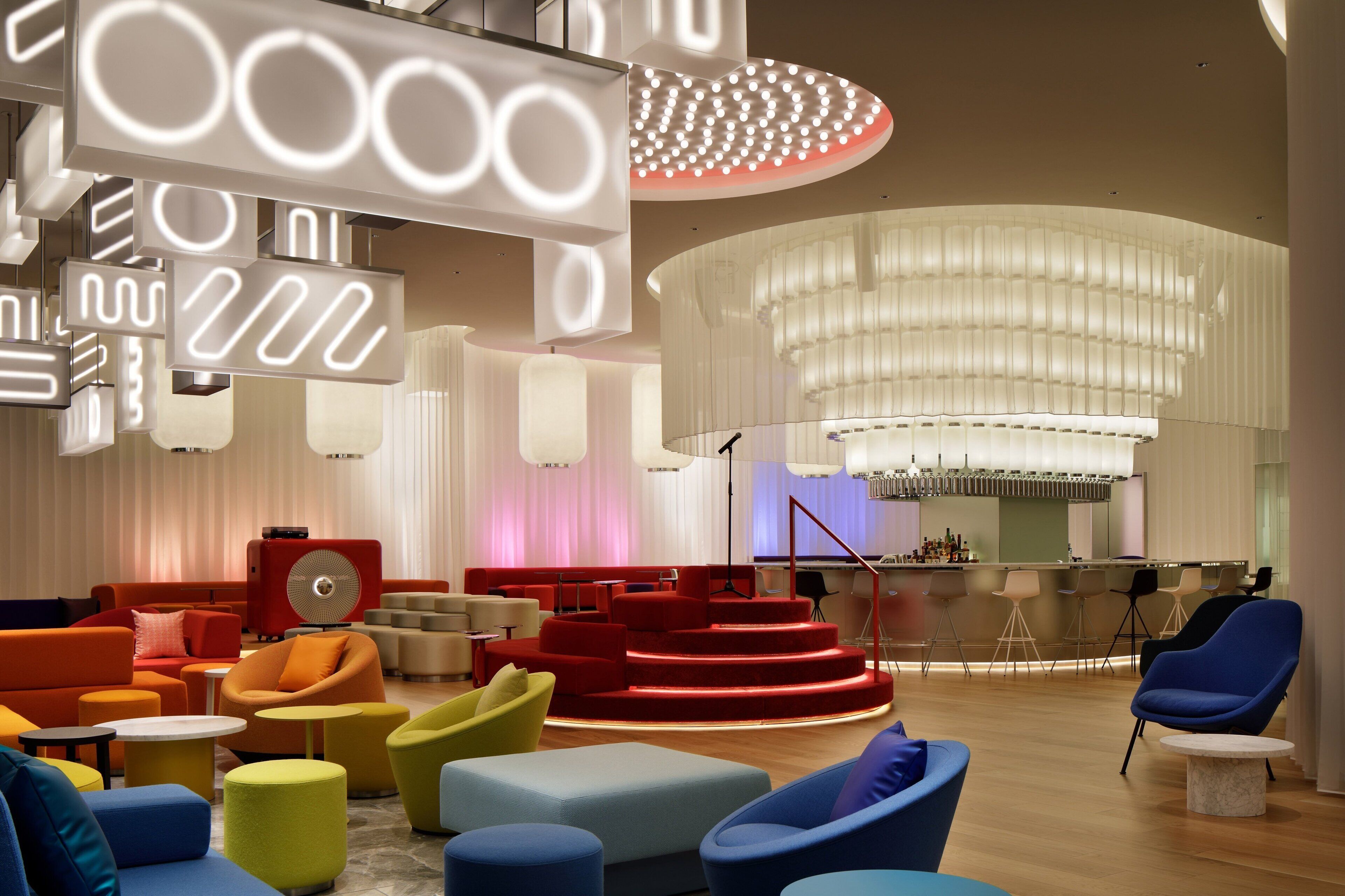 A modern lounge area with colorful seating, a bar, and a stage.