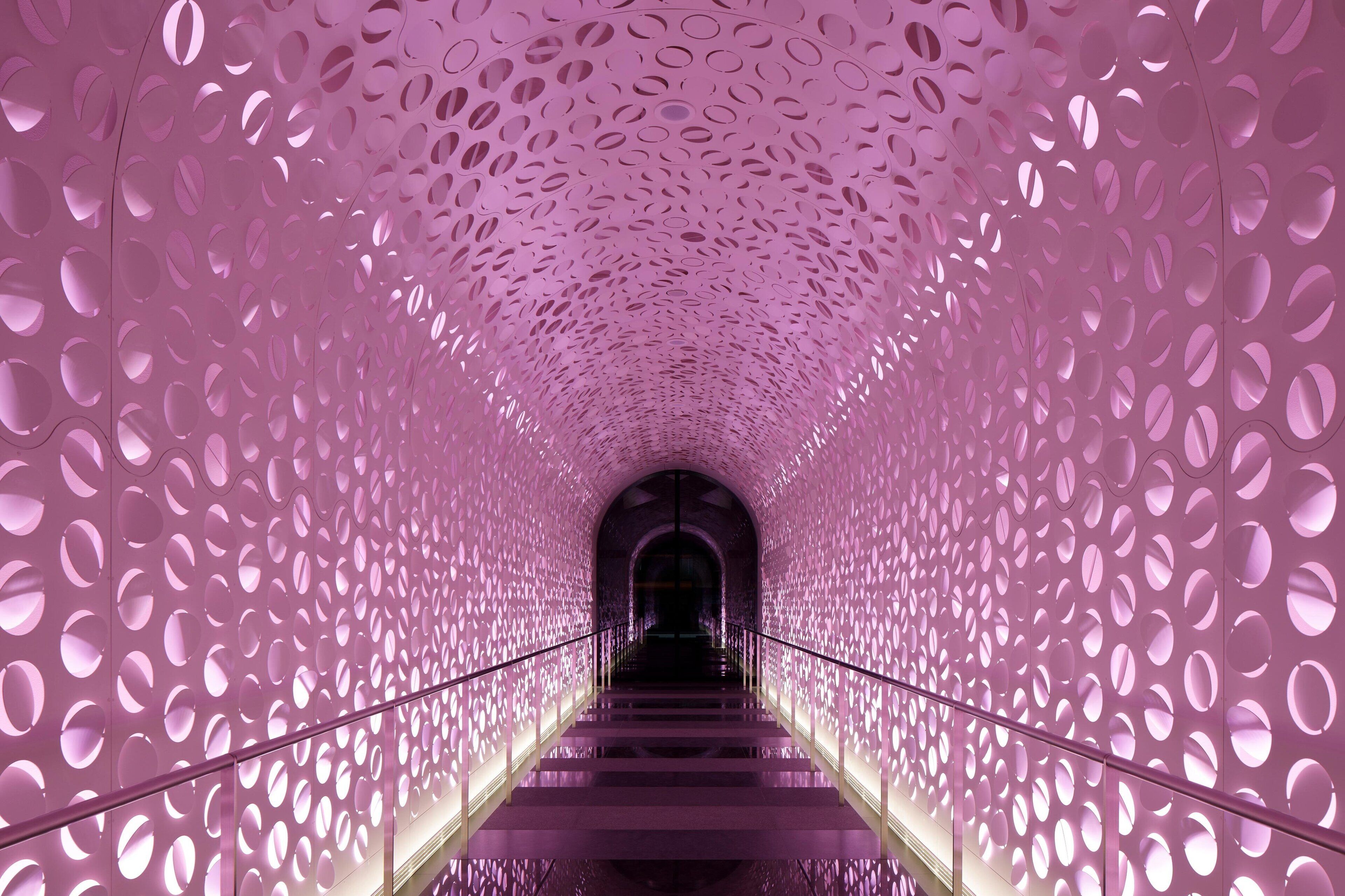 A corridor with a patterned ceiling and walls, leading to a dark doorway.