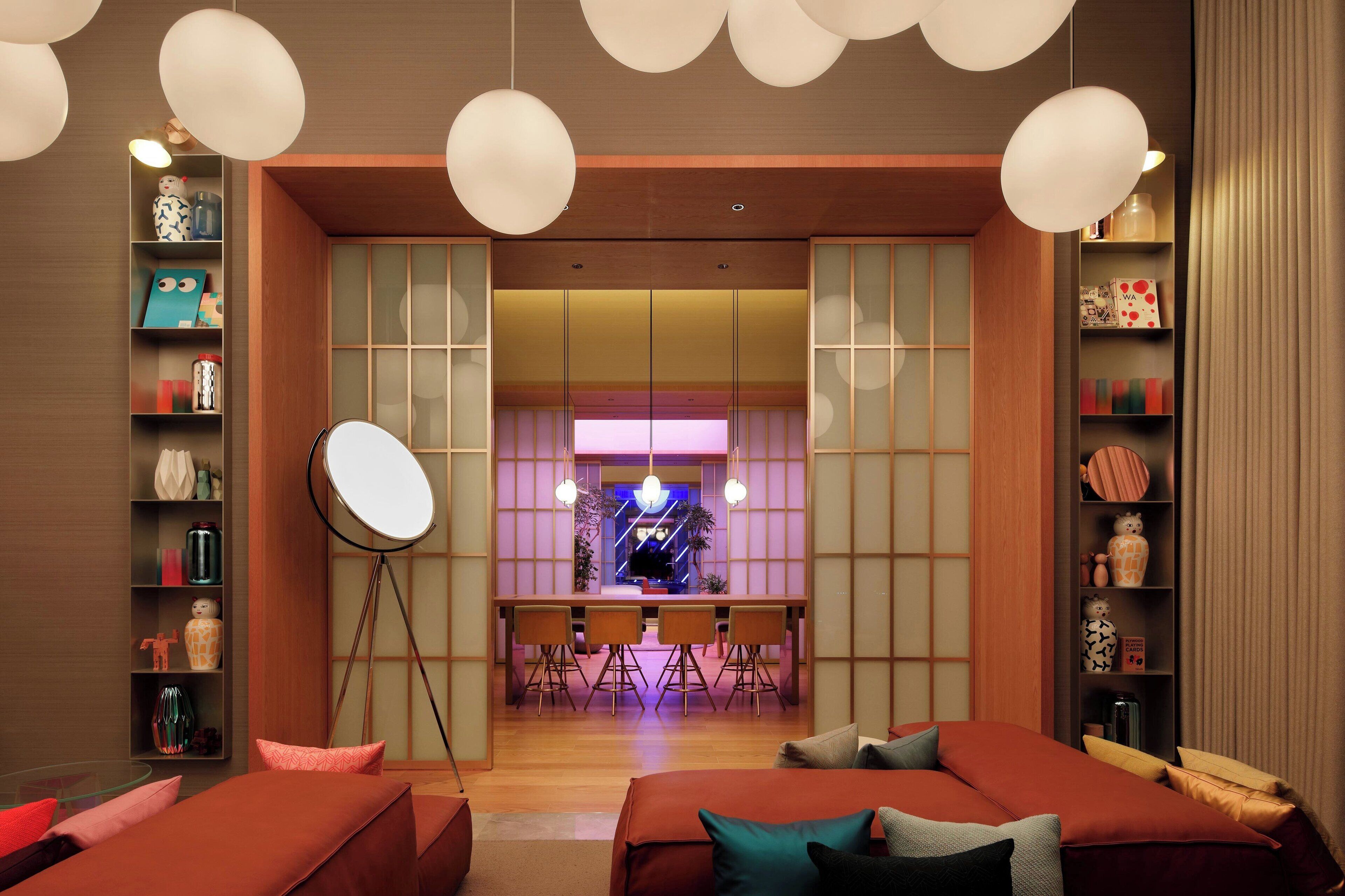 A modern hotel room with a dining area, a large round mirror, and a variety of decorative items on shelves.