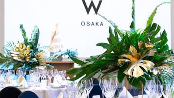 A table set for a formal event with clear glassware and white napkins, surrounded by lush tropical foliage.