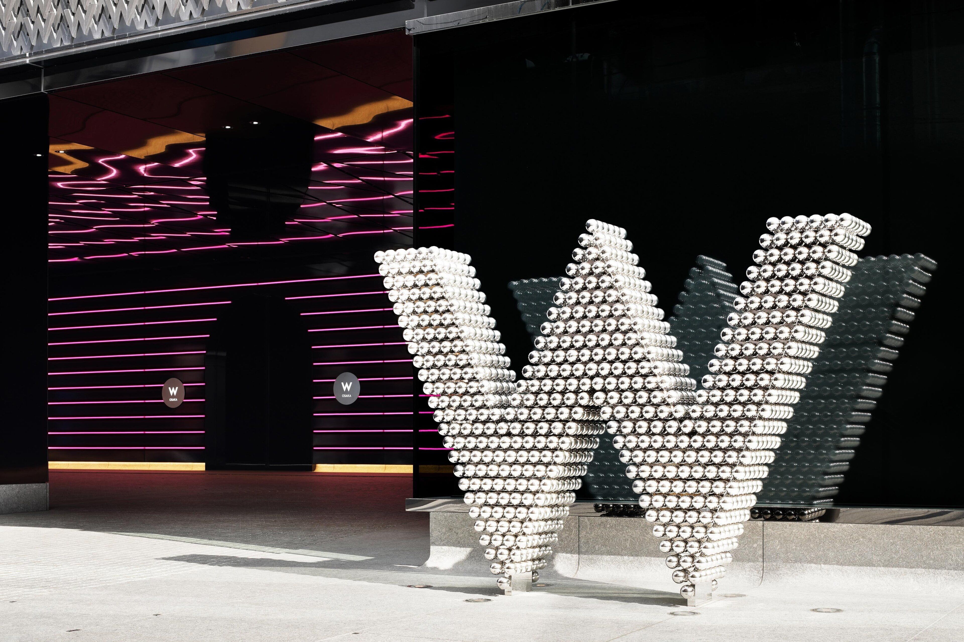 A modern building facade with neon lights and a unique sculpture made of cylindrical objects.