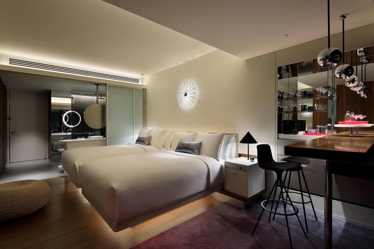 A modern bedroom with a large bed, bedside tables, a desk with a chair, a round wall clock, and a mirror with decorative elements.