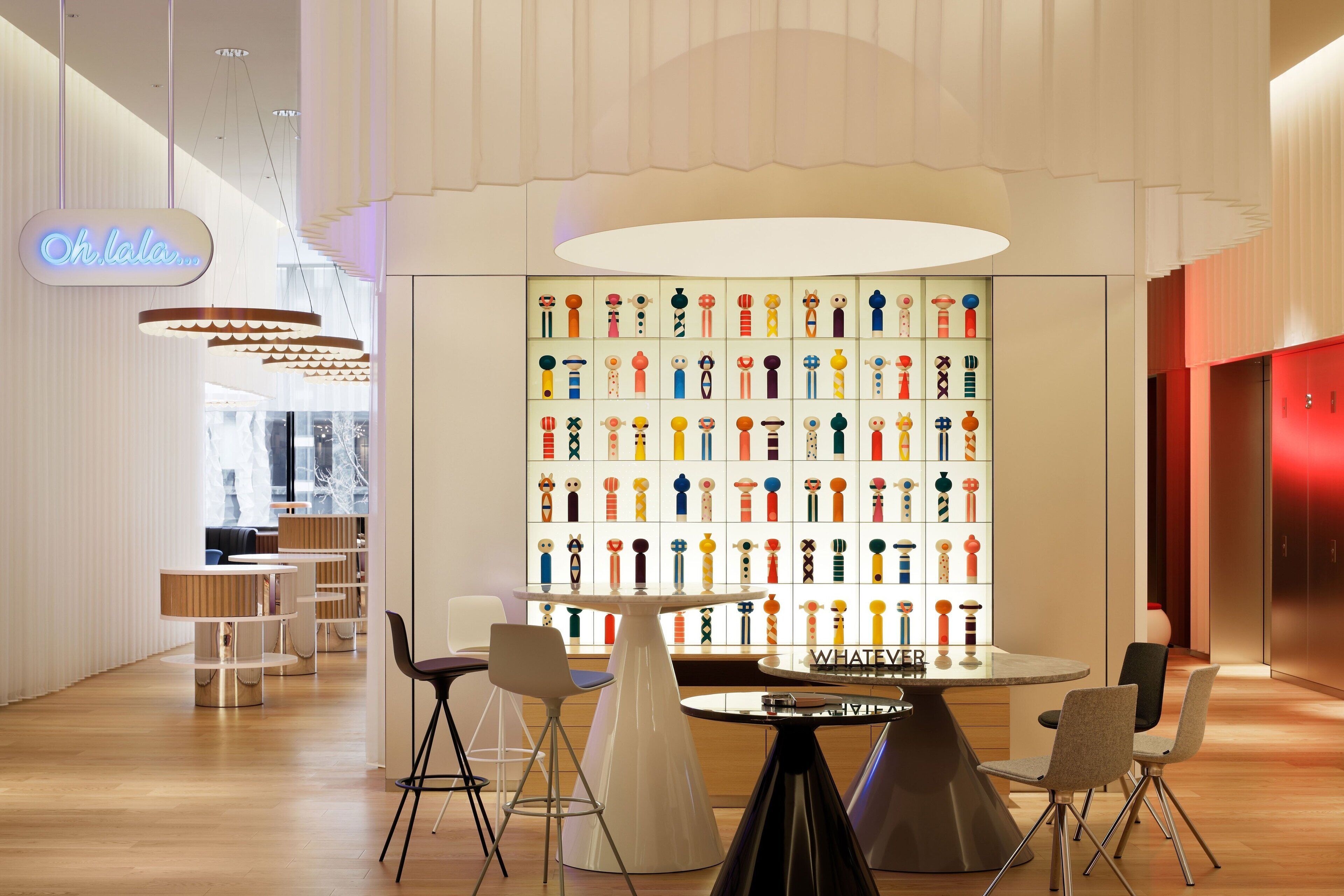 A modern interior with a central table surrounded by chairs, a wall of colorful figurines, and a neon sign.