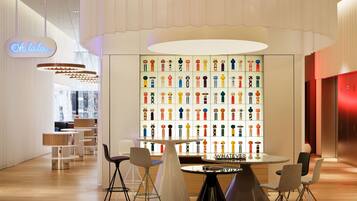 A modern interior with a central table surrounded by chairs, a wall of colorful figurines, and a neon sign.