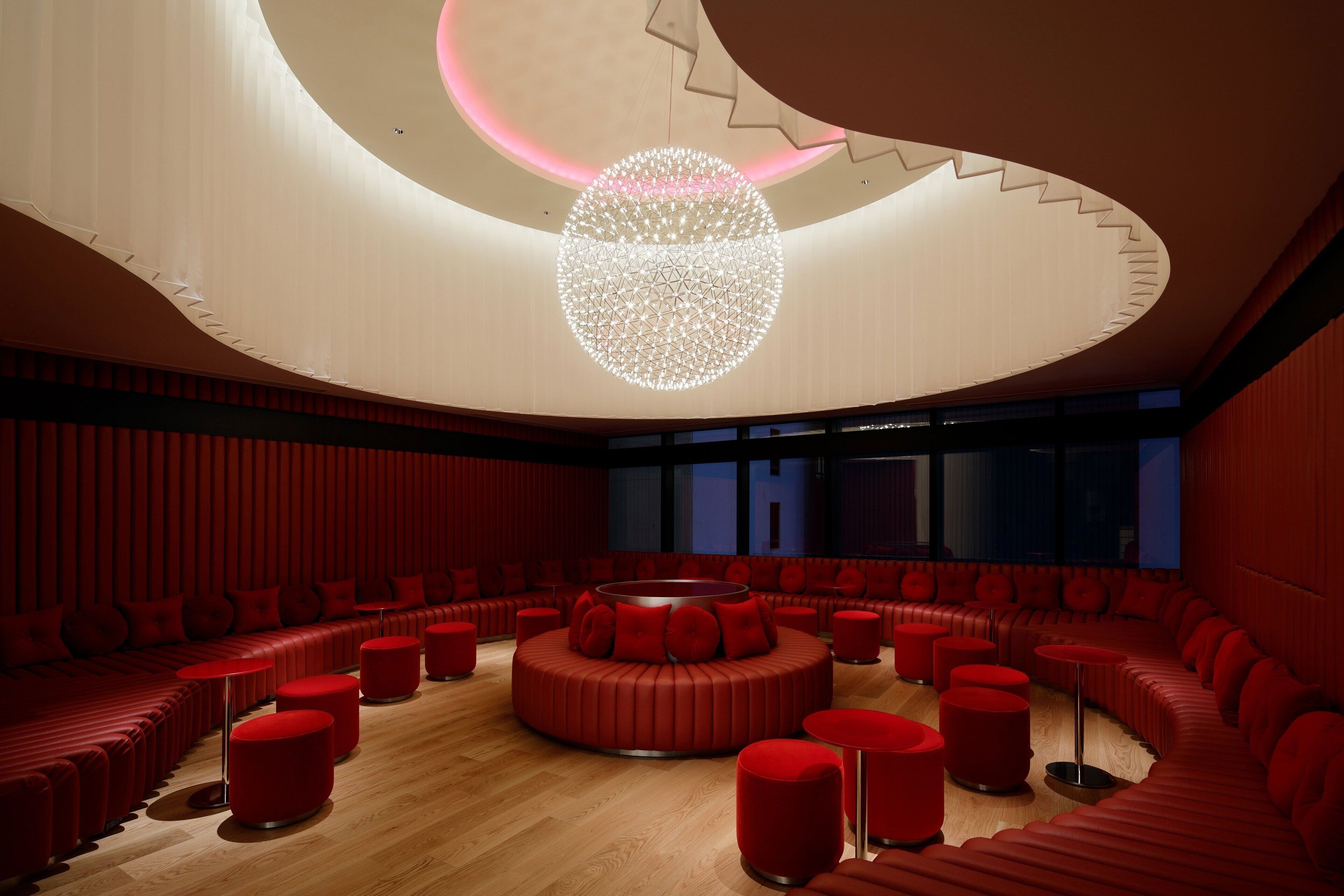 A modern interior with a circular seating area, a unique ceiling design, and a large window in the background.