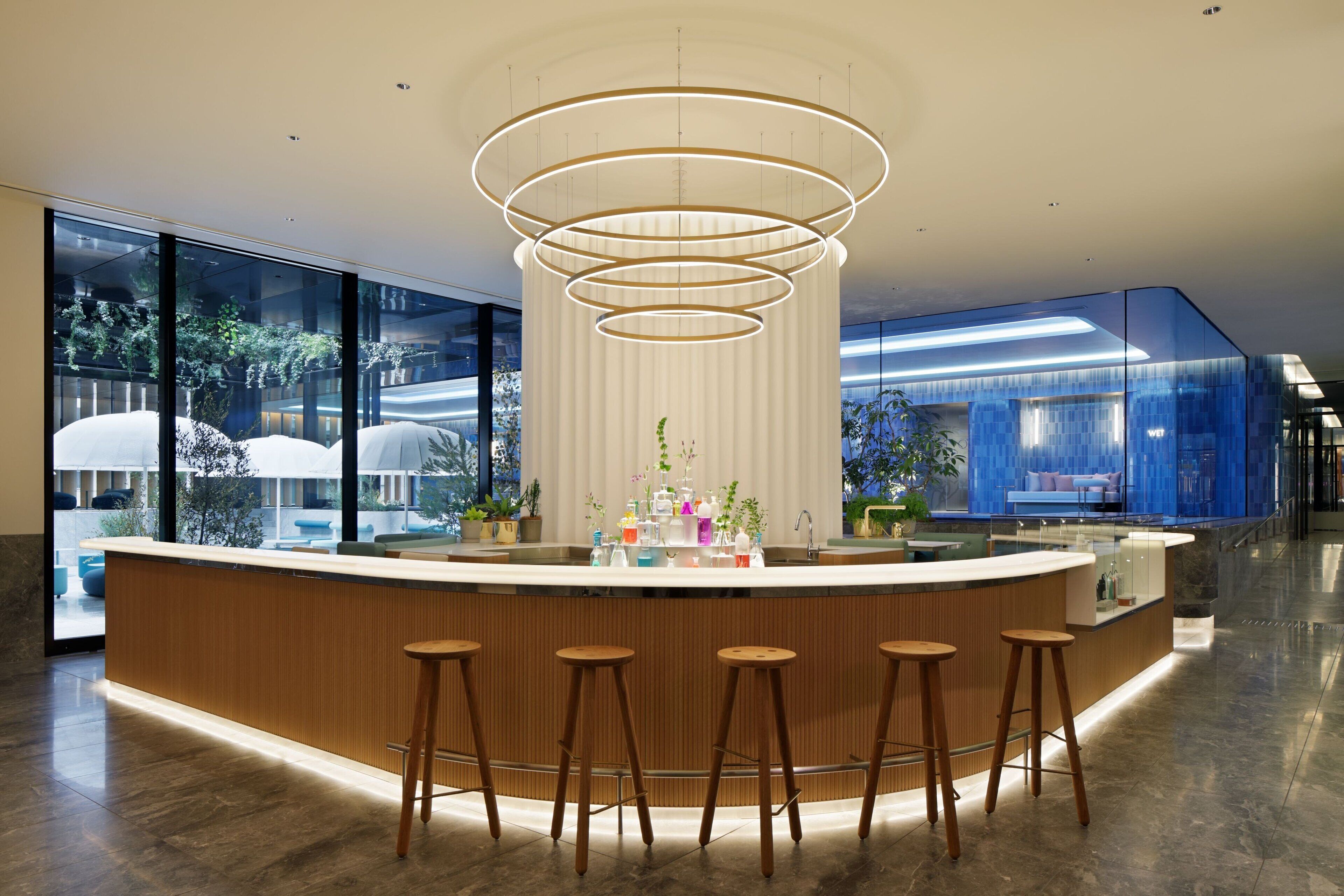 A modern bar area with a central light fixture, a wooden counter, and four stools.
