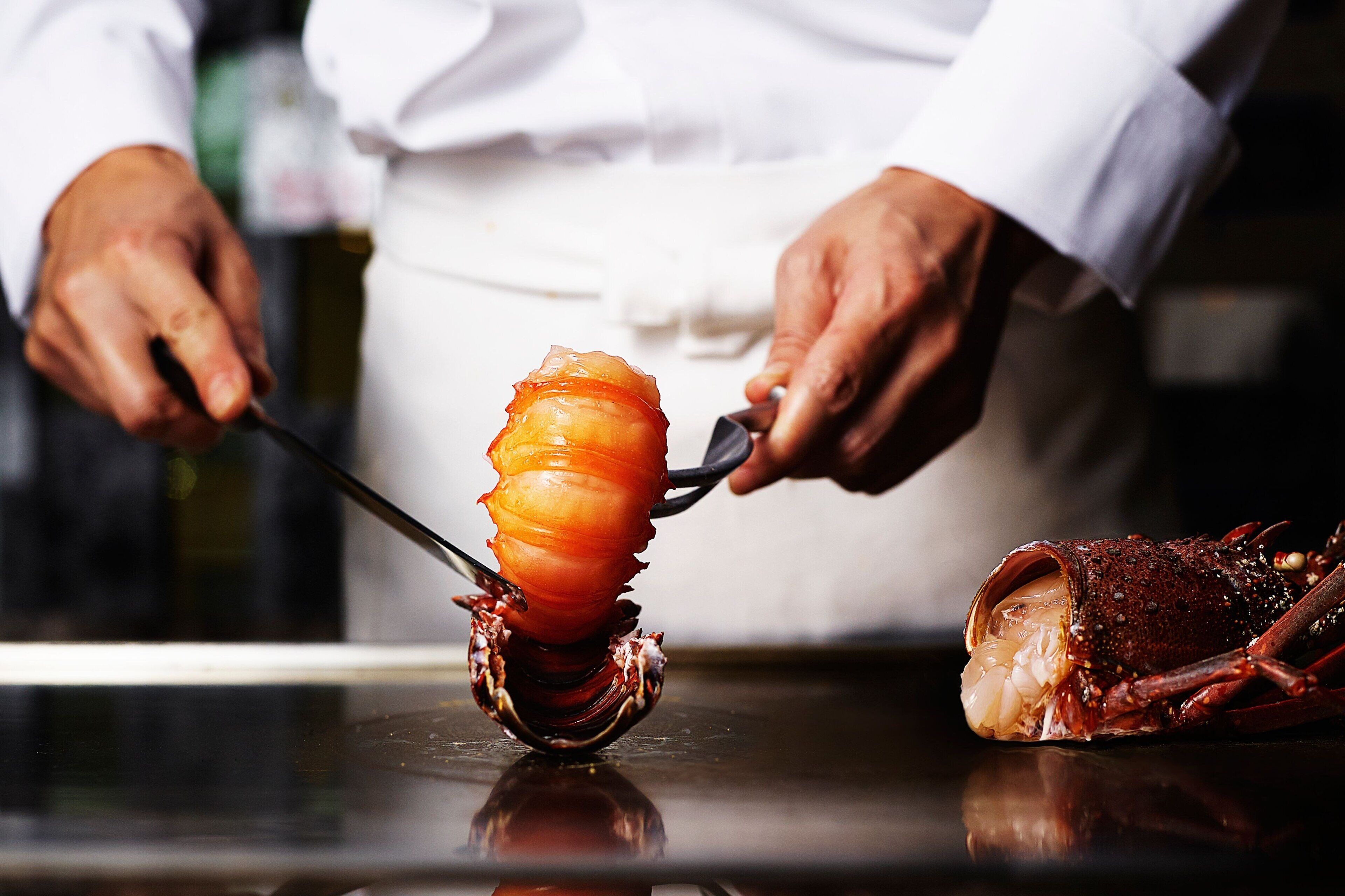 A chef carving a large, cooked meat with a carving fork.