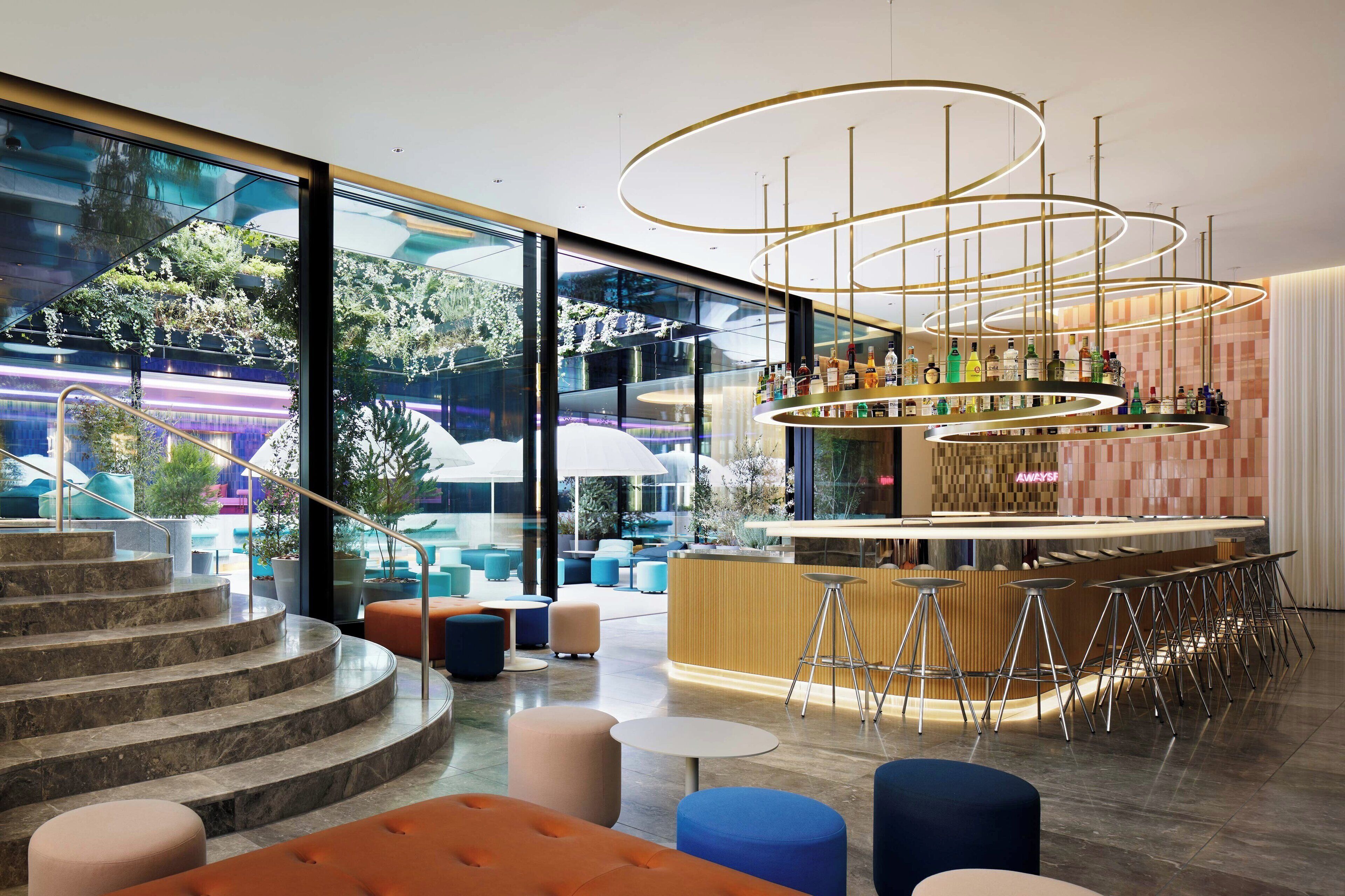 A modern bar area with a circular bar counter, stools, and a view of outdoor seating and greenery.