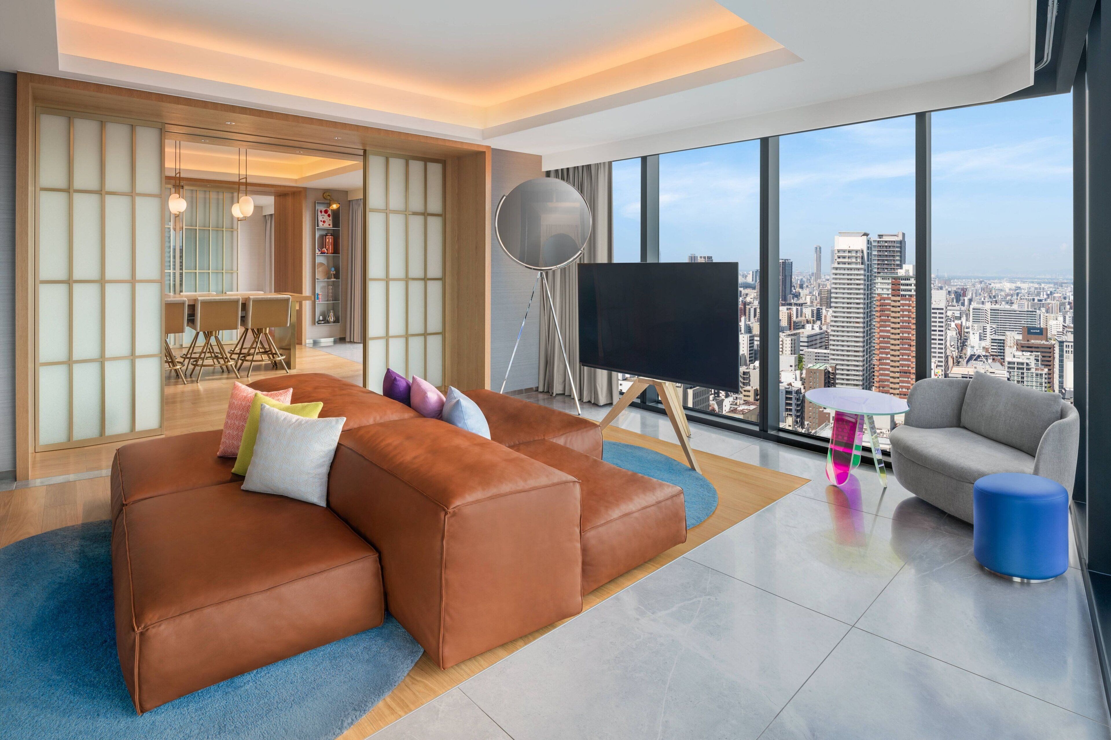 A modern living room with a brown leather sofa, a grey armchair, and a TV on a tripod stand.