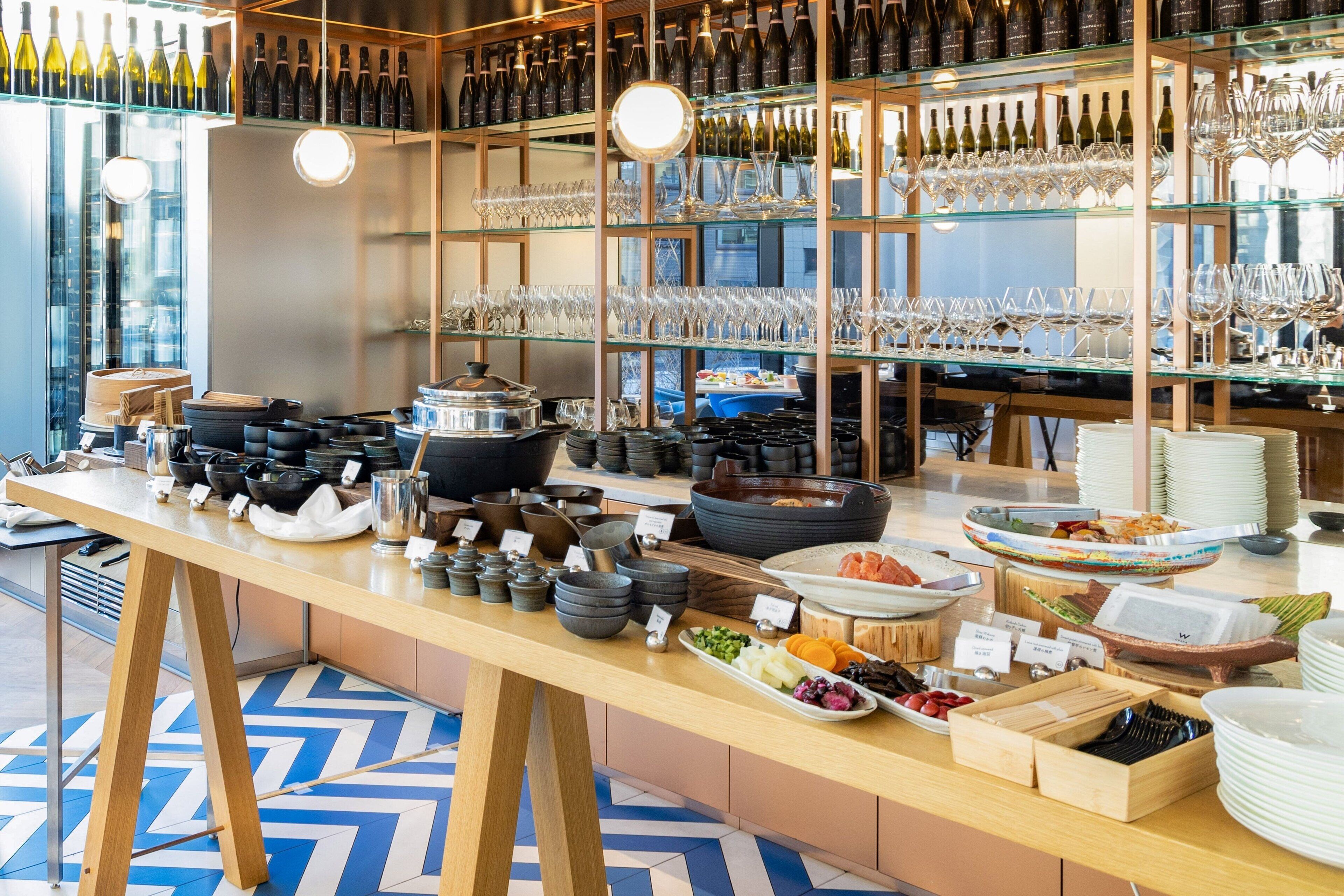 Zona de bufé con diversos platos, cuencos y botellas de vino.