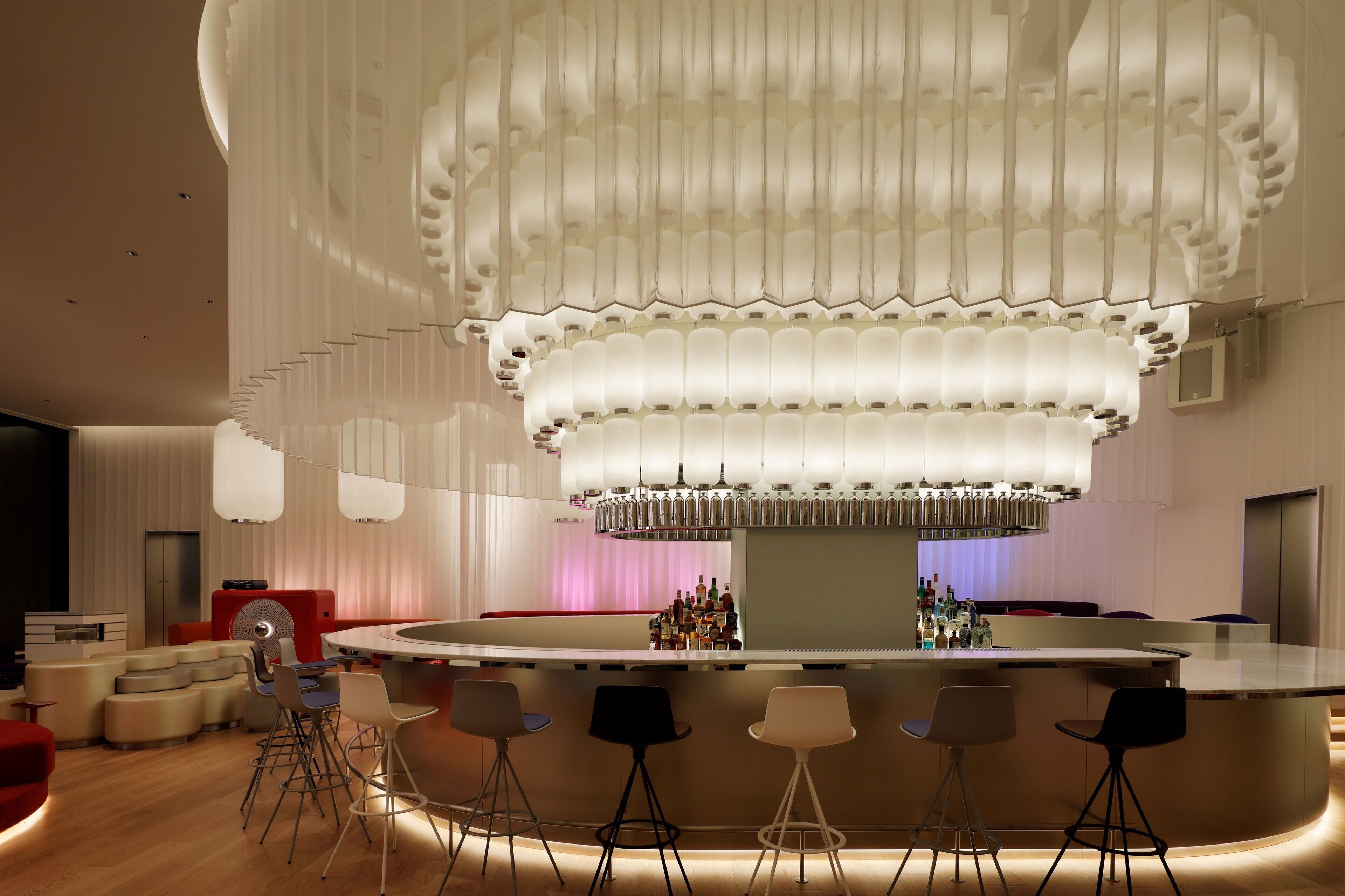 A modern bar area with a central bar counter, multiple seating options, and a distinctive ceiling design.