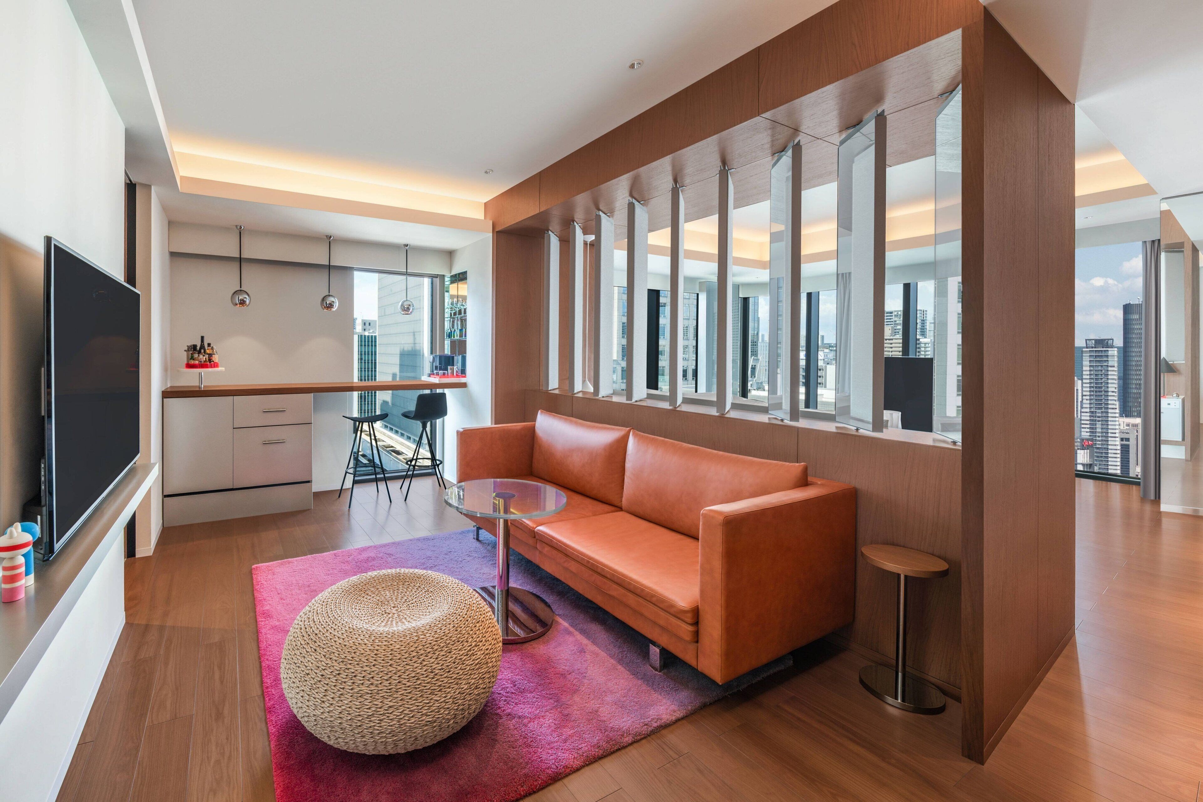 A modern living room with a leather sofa, a round coffee table, and a woven pouf.