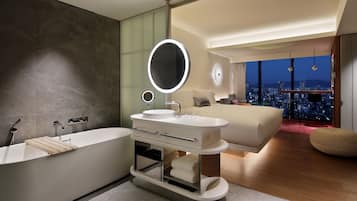 A modern bedroom with a large bed, a vanity with a mirror, and a view of a cityscape at night.