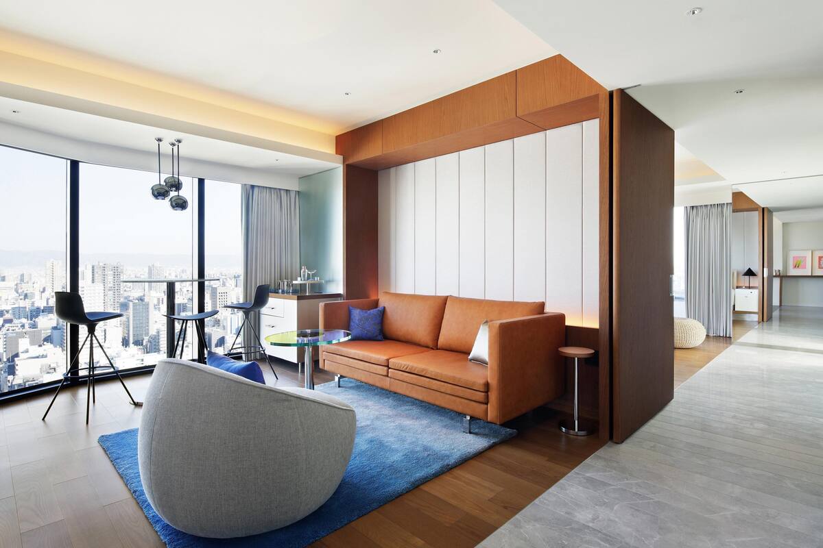 A modern living room with a large window, a sofa, a chair, and a small table.
