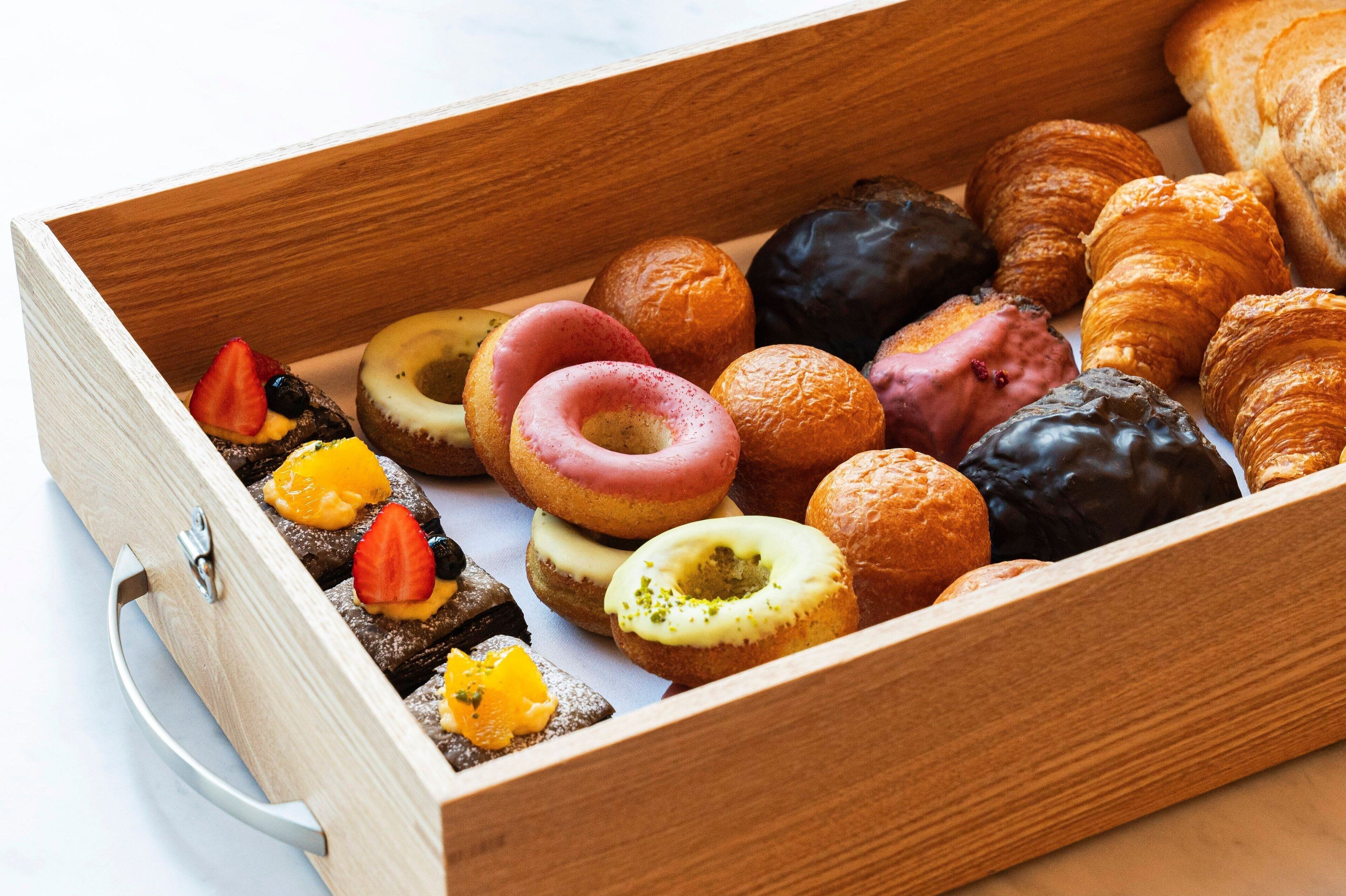 A wooden box filled with various pastries and donuts.