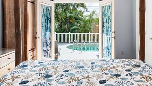 Une chambre avec un lit, donnant sur une piscine, et une clôture blanche.