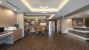 Un hall d’hôtel moderne avec un comptoir d’accueil, un espace salon et un grand lustre.