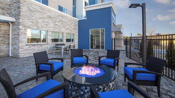 Un espace patio avec une table ronde et des chaises, un foyer extérieur et un bâtiment à la façade en pierre agrémentée de touches de bleu.