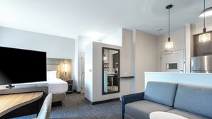 Une chambre d’hôtel moderne équipée d’une télévision à écran plat, d’un canapé, d’une petite table, d’un lit et d’un coin cuisine.